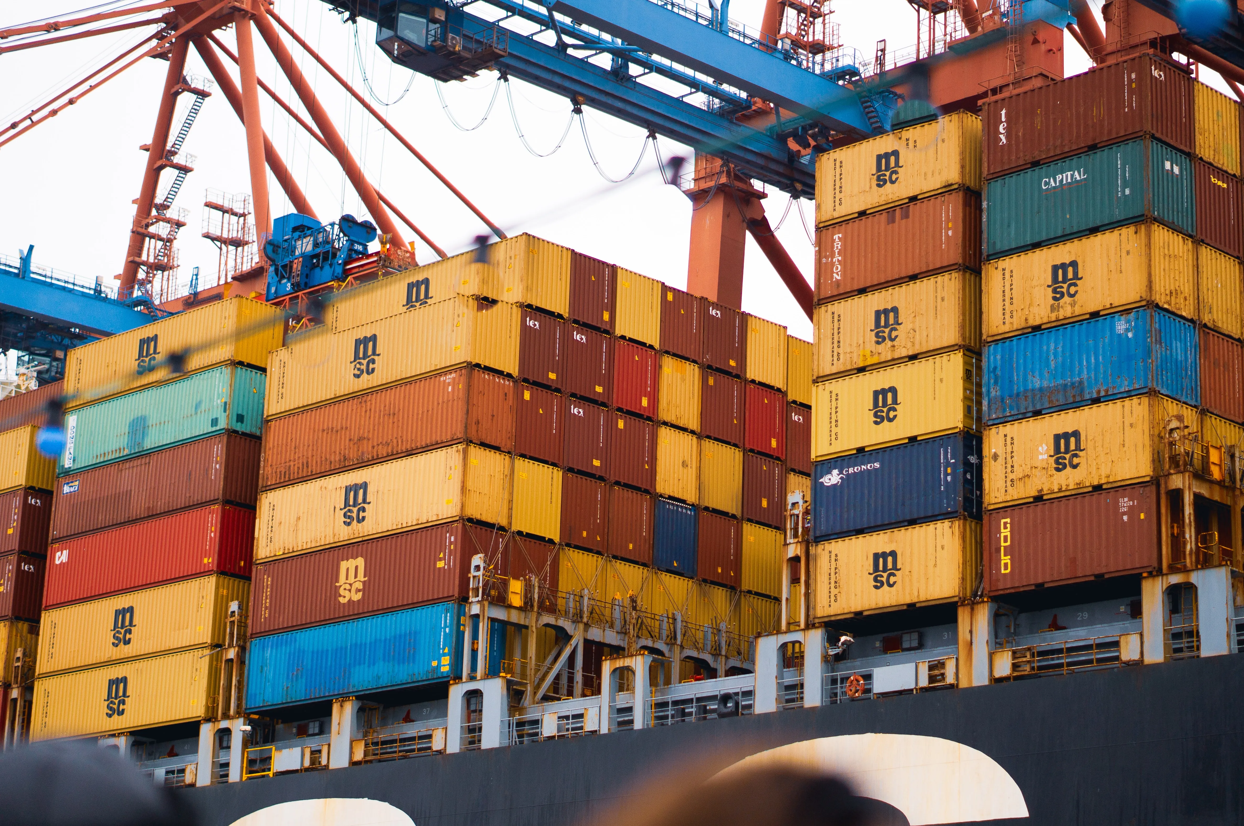 Yellow, blue, red and orange containers being loaded onto a cargo ship.