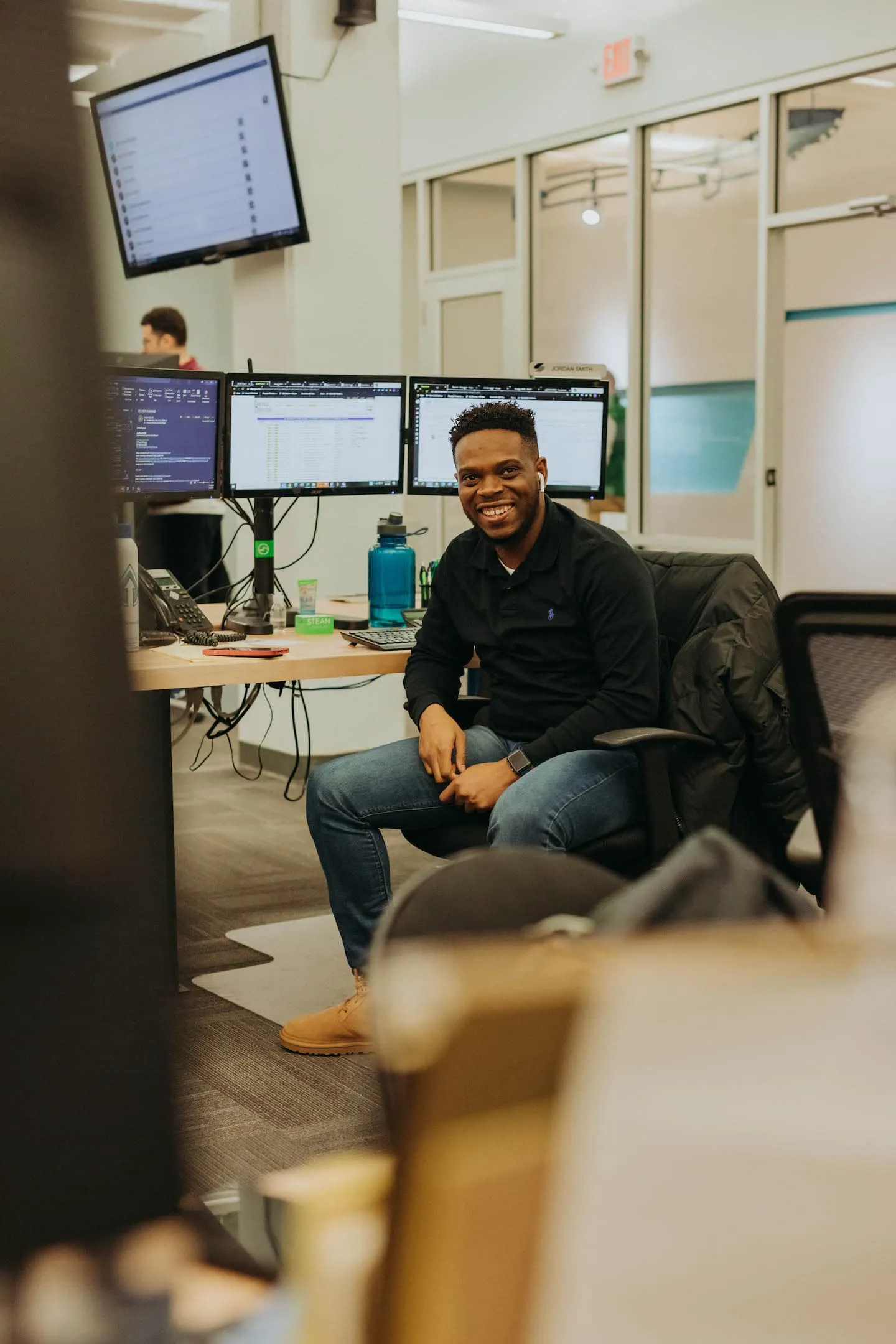 A Steam Logistics employee sits at his workstation, equipped with three monitors.